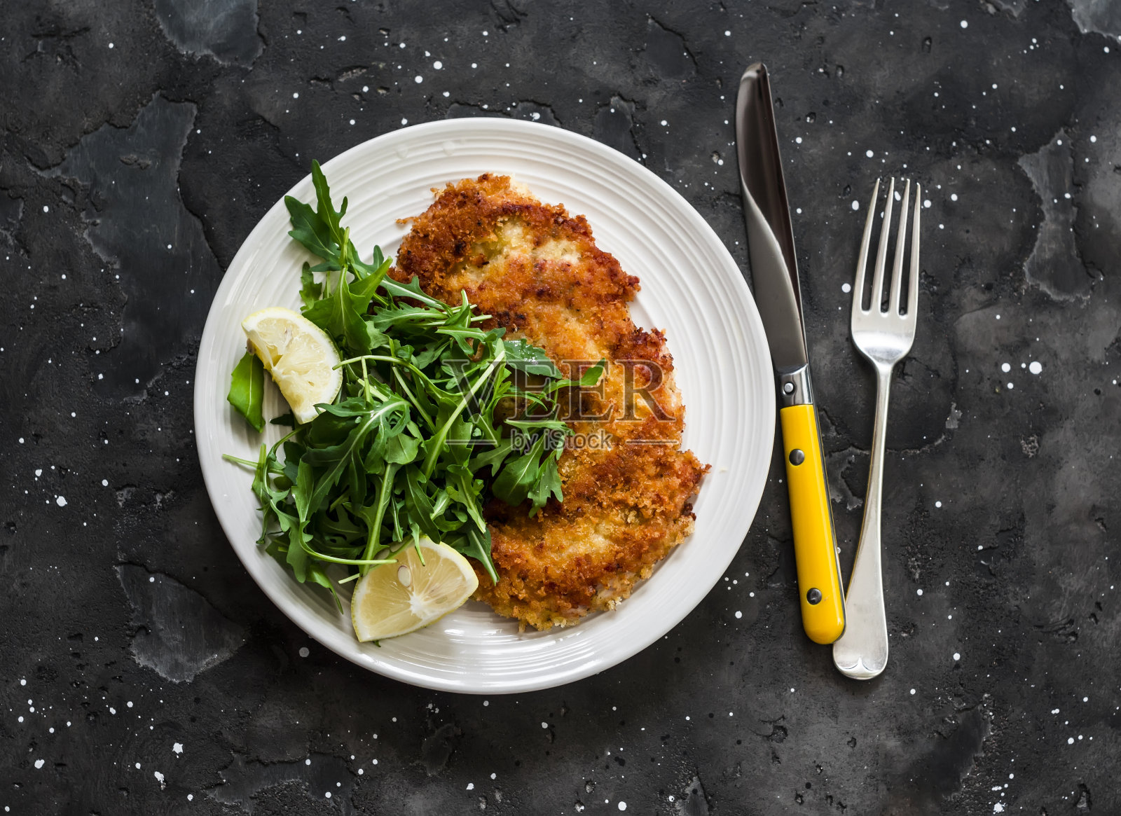 蒜香面包屑、酥脆的火鸡肉排和新鲜的柠檬芝麻菜沙拉，背景为黑色，俯视图照片摄影图片