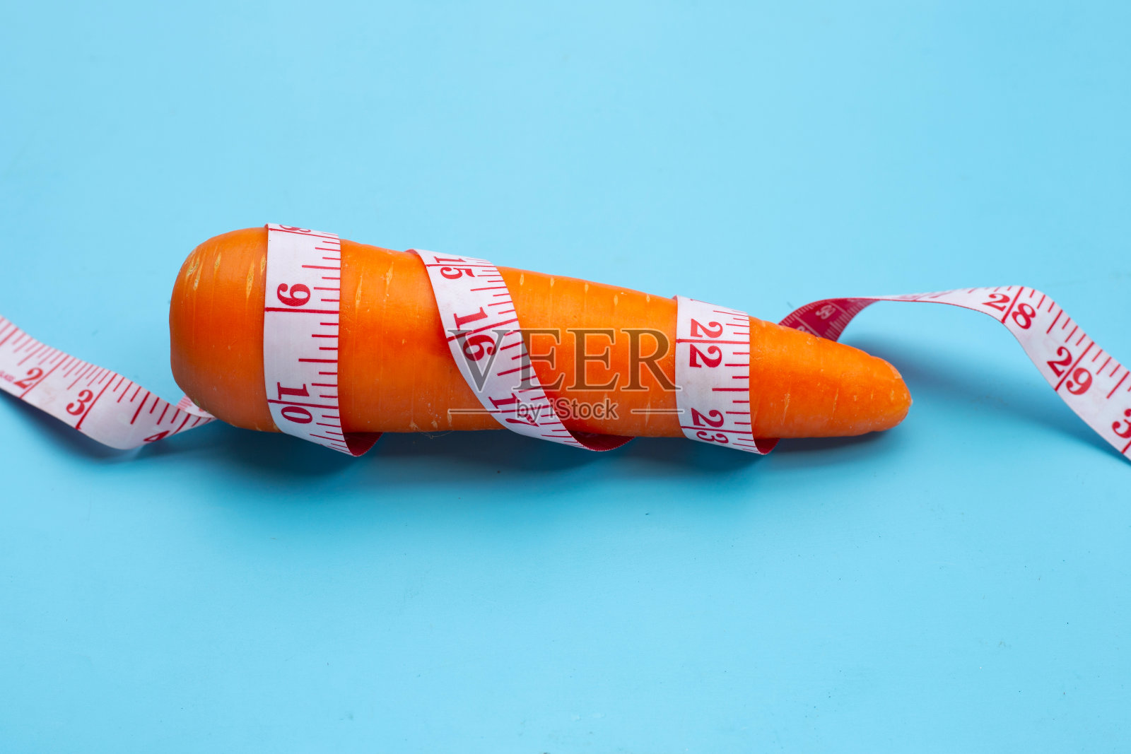 胡萝卜用卷尺包裹在蓝色背景上。照片摄影图片