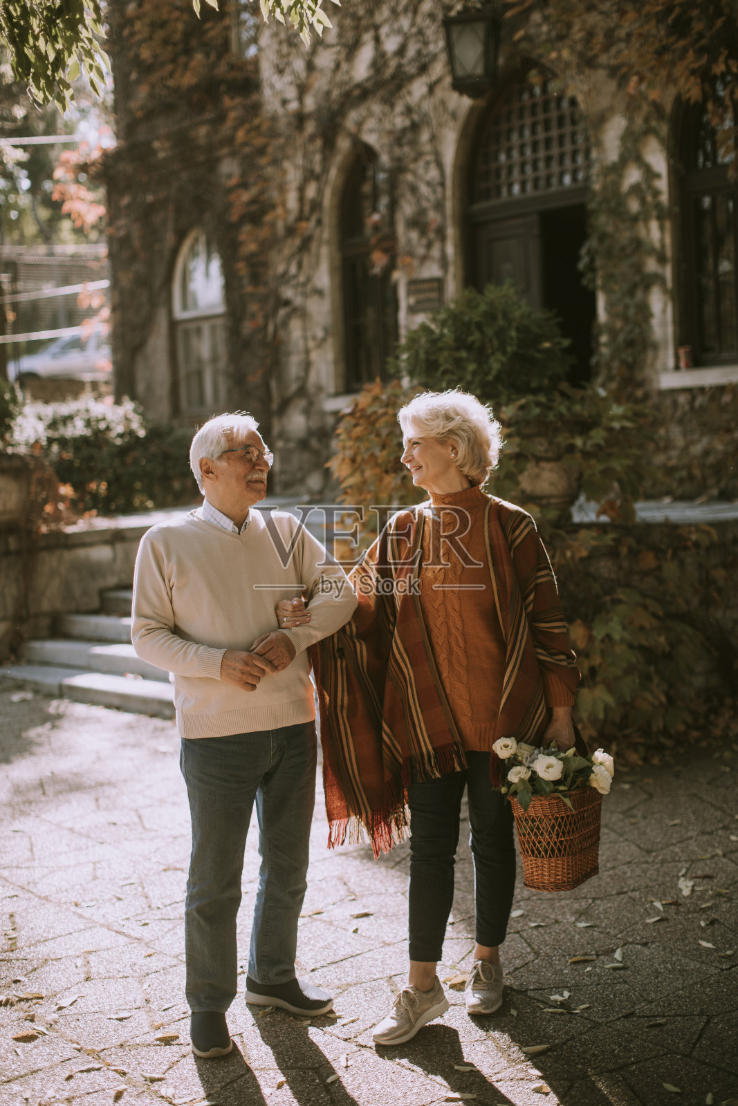 一对老年夫妇带着装满鲜花和杂货的篮子走在秋天的公园里照片摄影图片