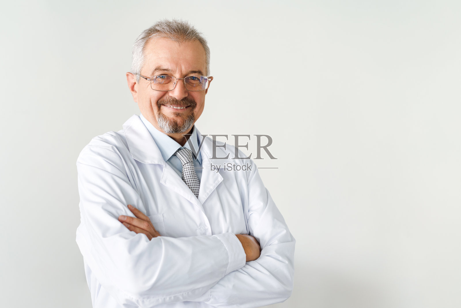 一位上了年纪的男医生在白色背景上的肖像。友好的医生一边看着镜头一边微笑照片摄影图片