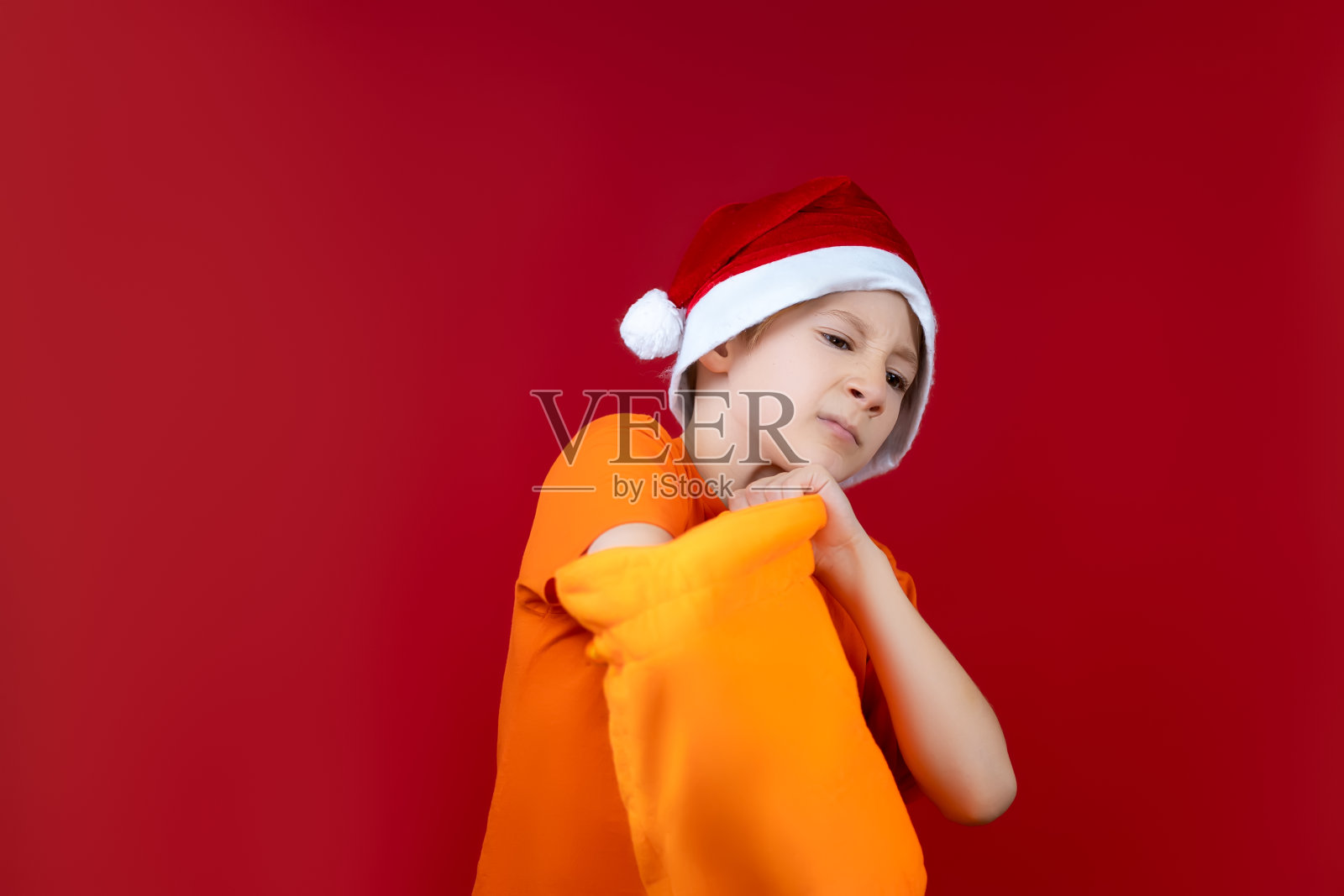 一个在红色圣诞背景上戴圣诞帽的男孩照片摄影图片