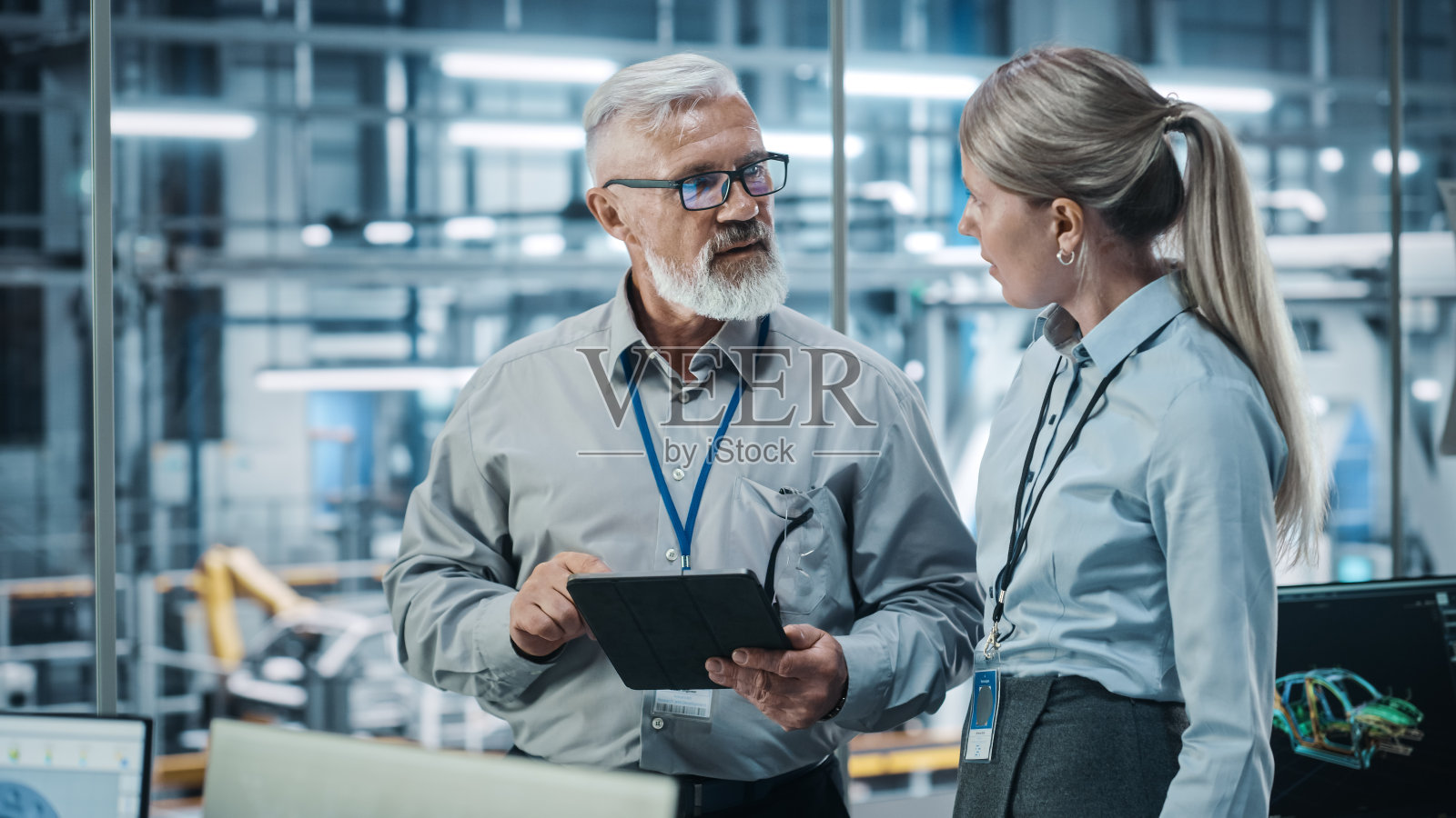 汽车工厂:女性项目经理与男性汽车工程师交谈，用平板电脑规划策略。自动化机器人手臂装配线生产输送机制造电动汽车照片摄影图片