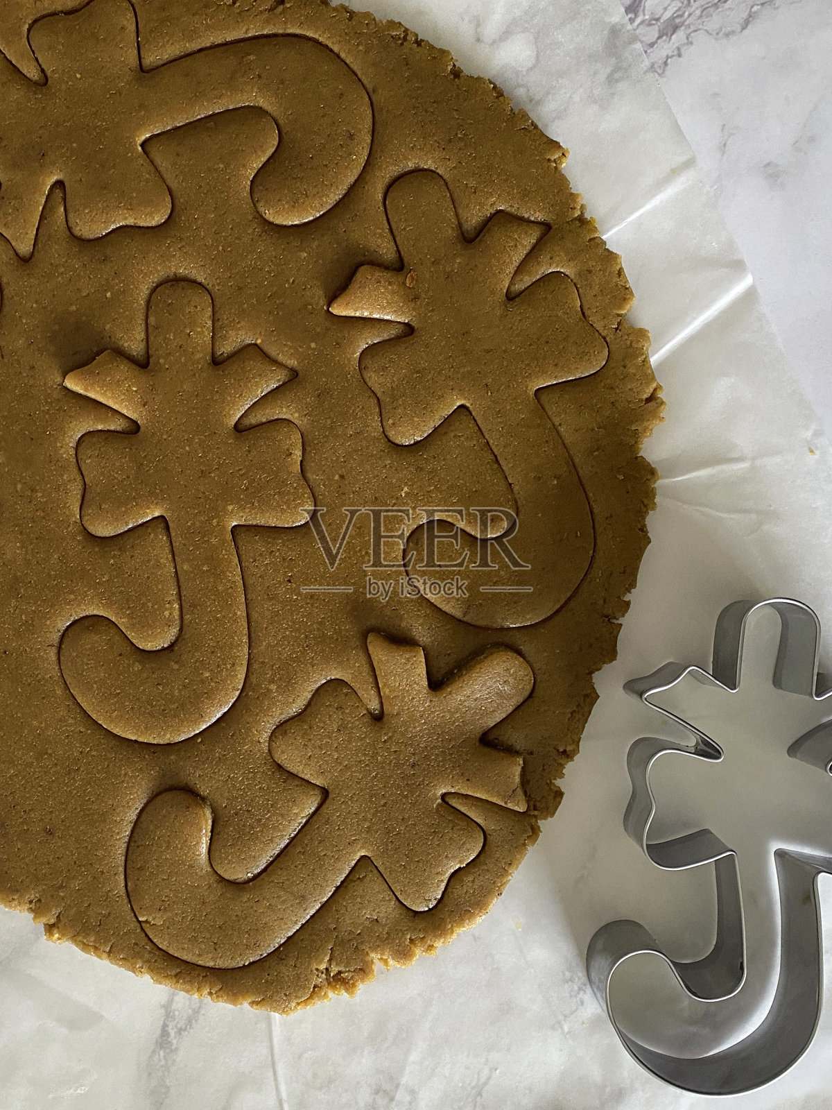 自制的姜饼曲奇面团用金属糖果甘蔗饼干切割器在防油羊皮纸上铺开，甘蔗用弓切出形状，家庭烘焙，高架视野照片摄影图片