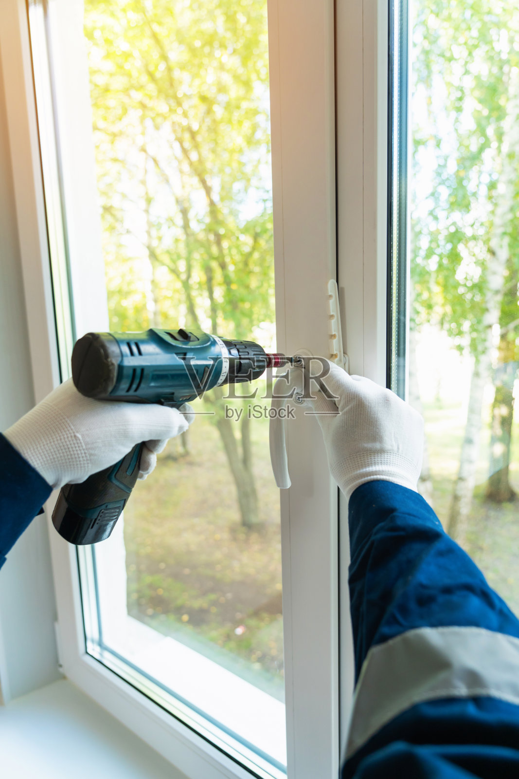 一名男子用电动螺丝刀在窗户上安装了一个白色塑料把手照片摄影图片