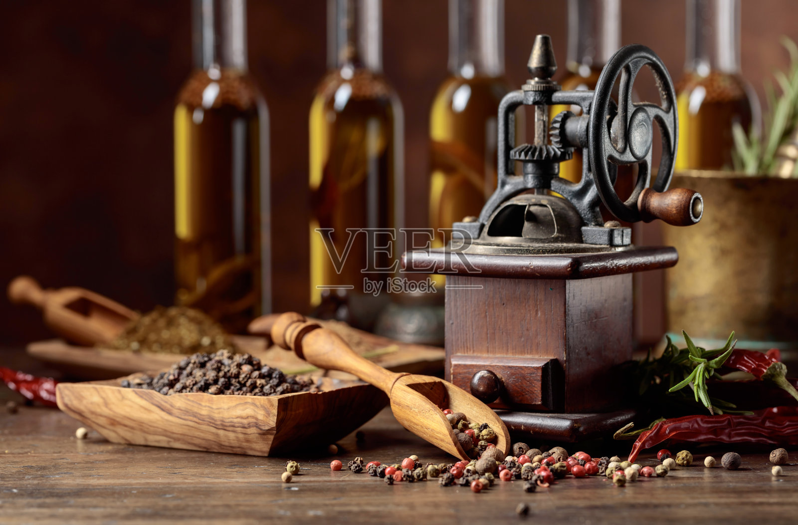 木桌上放着旧胡椒磨、烹饪器具、瓶装橄榄油、香料和迷迭香。照片摄影图片