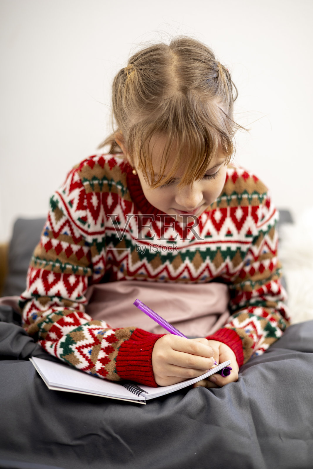 女孩许愿。孩子穿着圣诞睡衣坐在床上。照片摄影图片