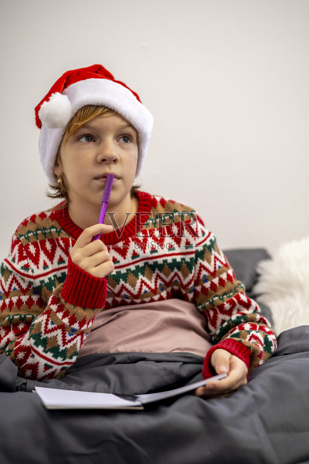 女孩许愿。孩子穿着圣诞睡衣坐在床上。照片摄影图片