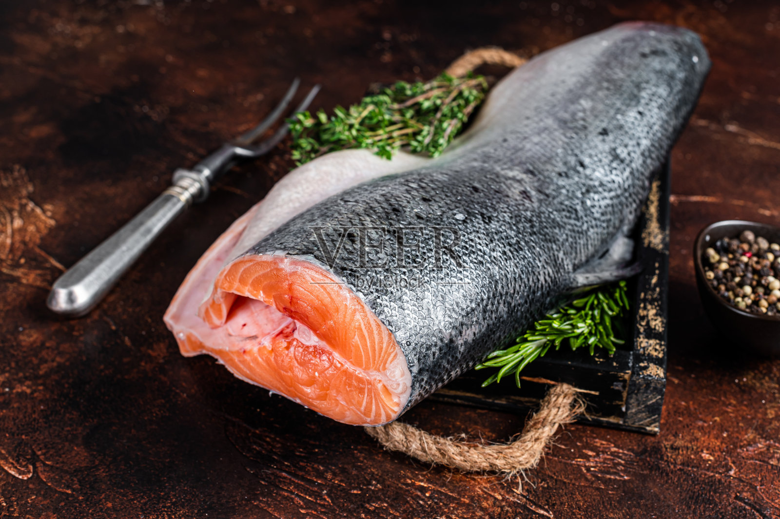 将生三文鱼切成片，放在木盘里，加入百里香。黑暗的背景。俯视图照片摄影图片