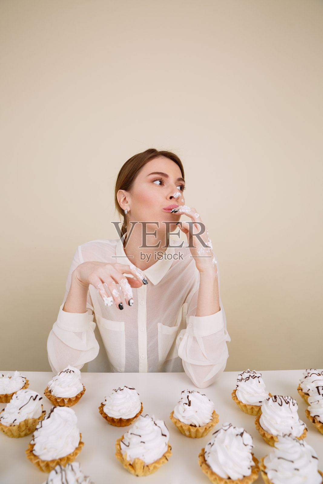 专心的年轻女士一边吃纸杯蛋糕一边摆姿势。照片摄影图片