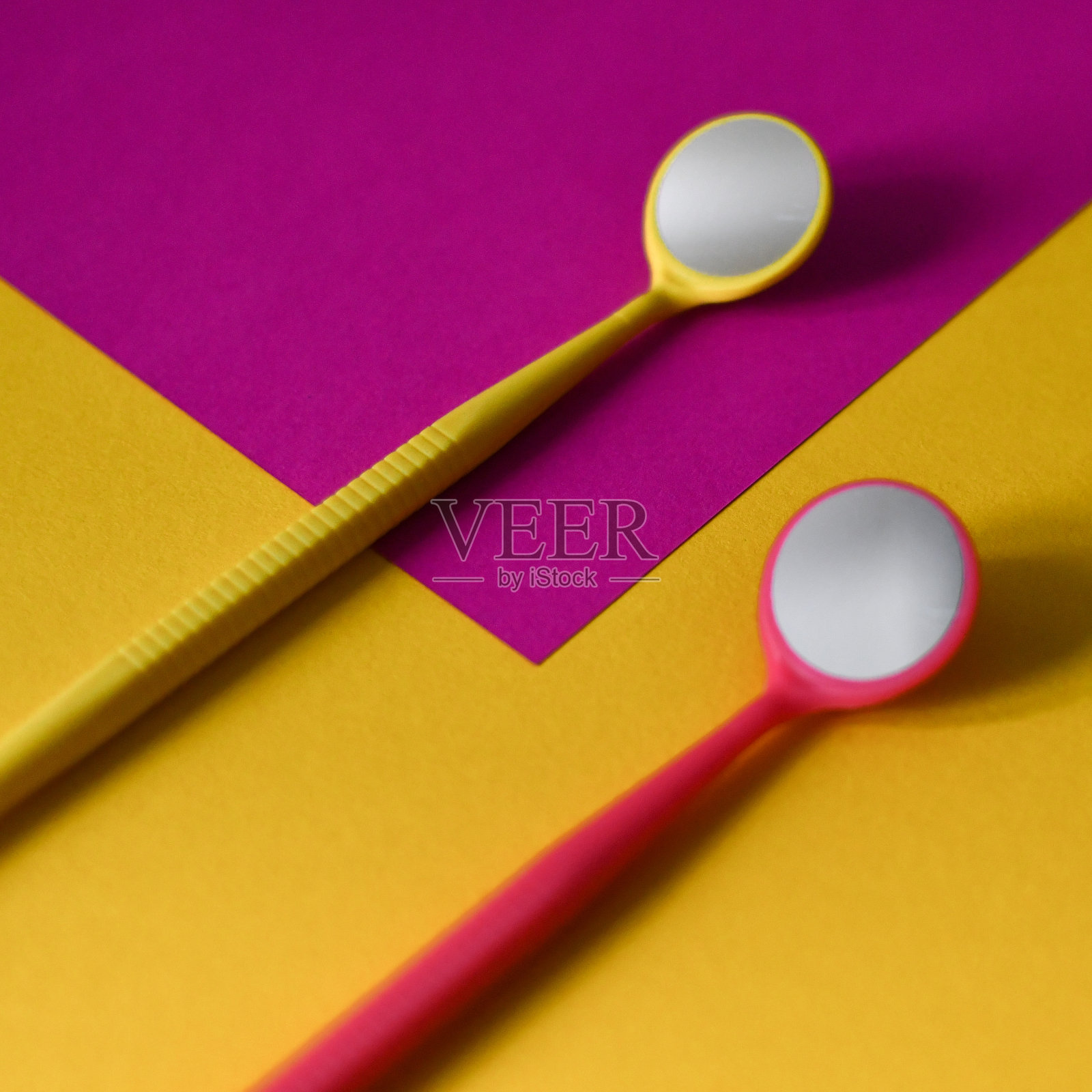 以黄色和粉红色为背景的两个牙科镜子的特写。本空间照片摄影图片