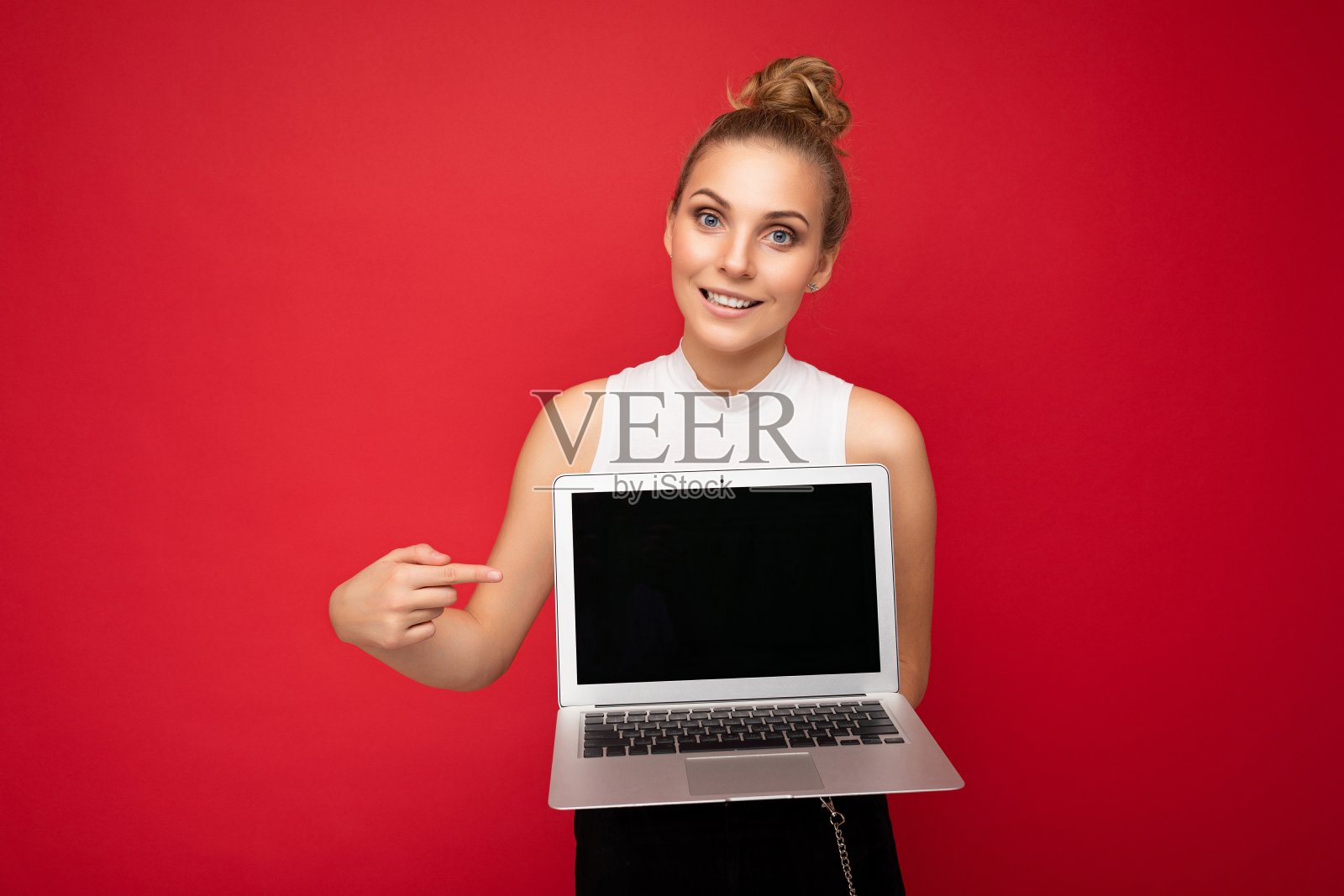 微笑快乐美丽迷人的深色金发年轻女学生妇女与聚集的头发看着相机持有电脑笔记本电脑与空的显示器屏幕与模拟和复制空间指着上网本键盘穿白色t恤照片摄影图片