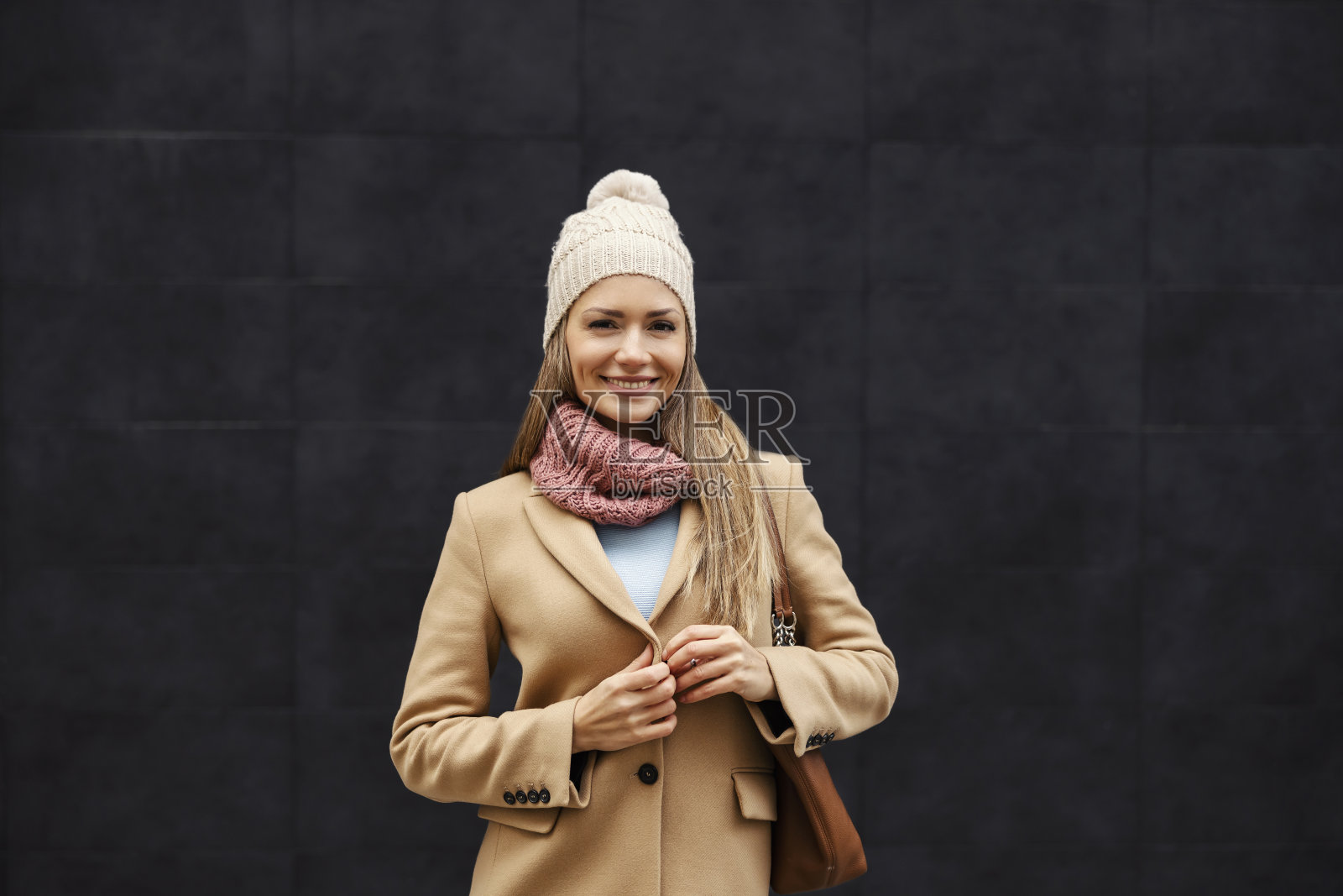 寒冷的天气里，一个穿着暖和衣服的快乐年轻女子站在户外，扣上她的暖和外套。时尚和寒冷的天气。一个穿着暖和衣服的女人。照片摄影图片