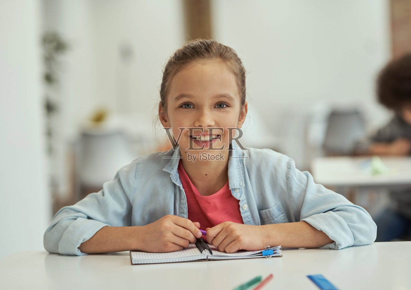 可爱的学生。漂亮的小女孩在相机微笑，而坐在教室的桌子上照片摄影图片