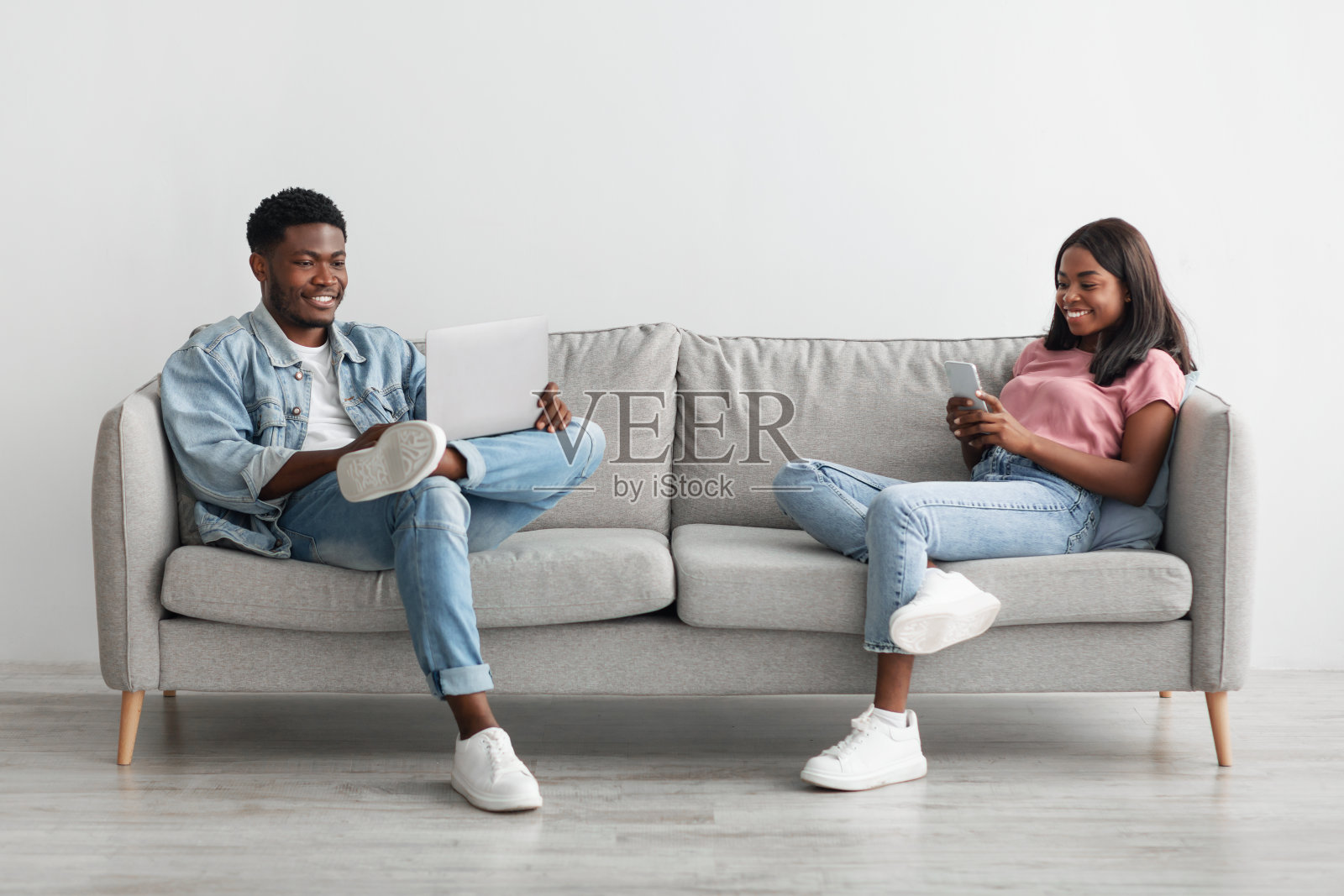 幸福的黑人夫妇坐在沙发上，用手机和电脑照片摄影图片