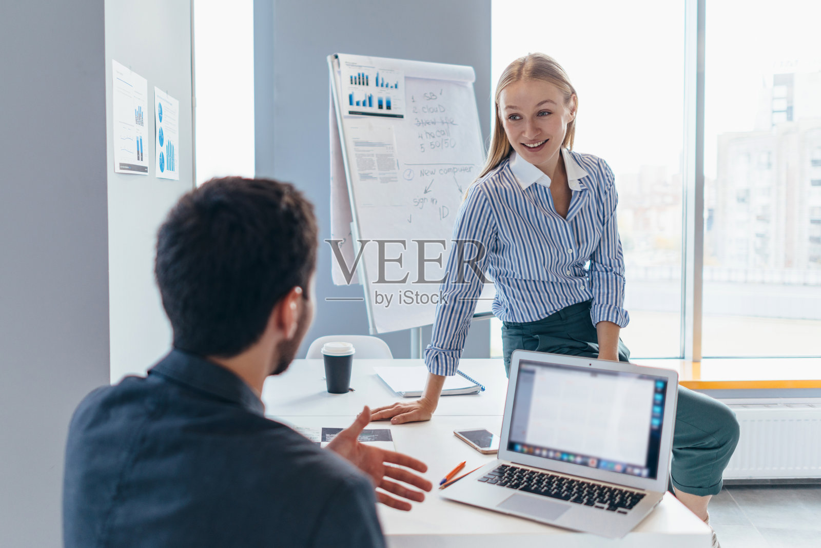 一位女士走到一位同事面前，坐在他的桌子上，愉快地和他说话照片摄影图片