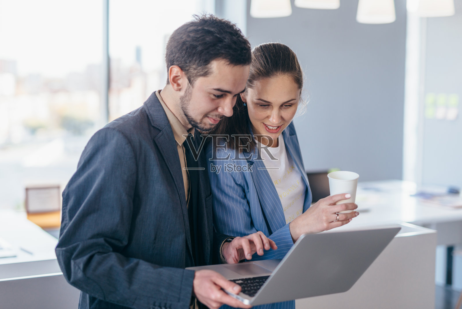 一男一女站在办公室里看着笔记本电脑屏幕照片摄影图片