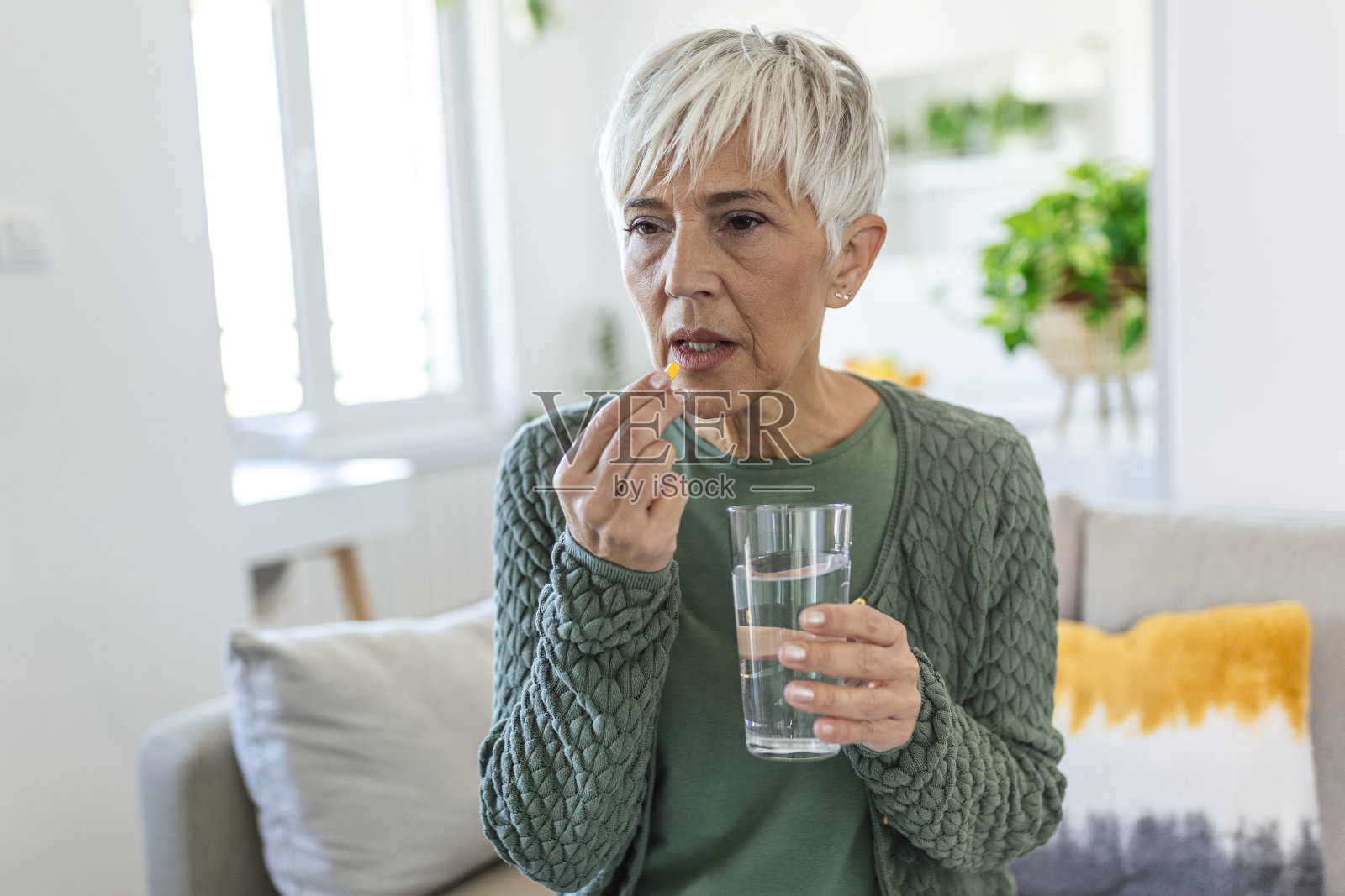 忍受着可怕的痛苦。成熟，悲伤，心烦，不开心，烦恼，灰发的虚弱女人，穿着休闲服坐在沙发上吃着药丸照片摄影图片
