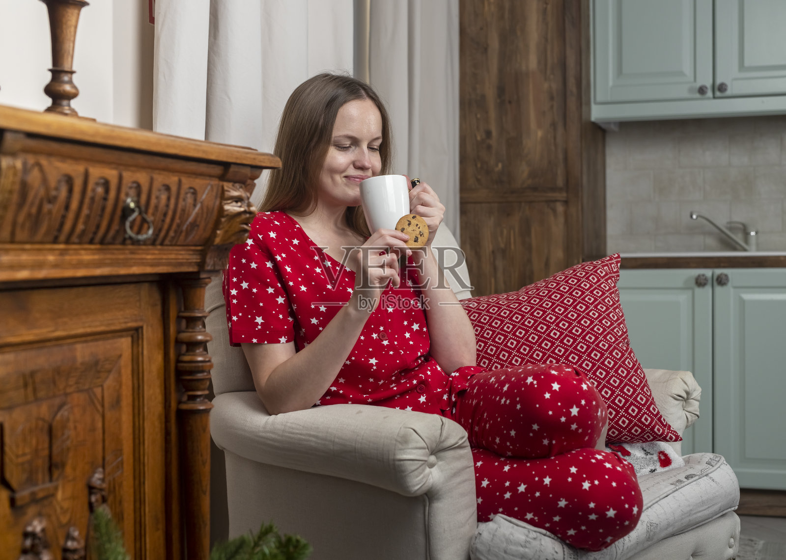 寒假里，一个女人手里拿着茶杯和饼干，坐在舒适的家里的椅子上照片摄影图片