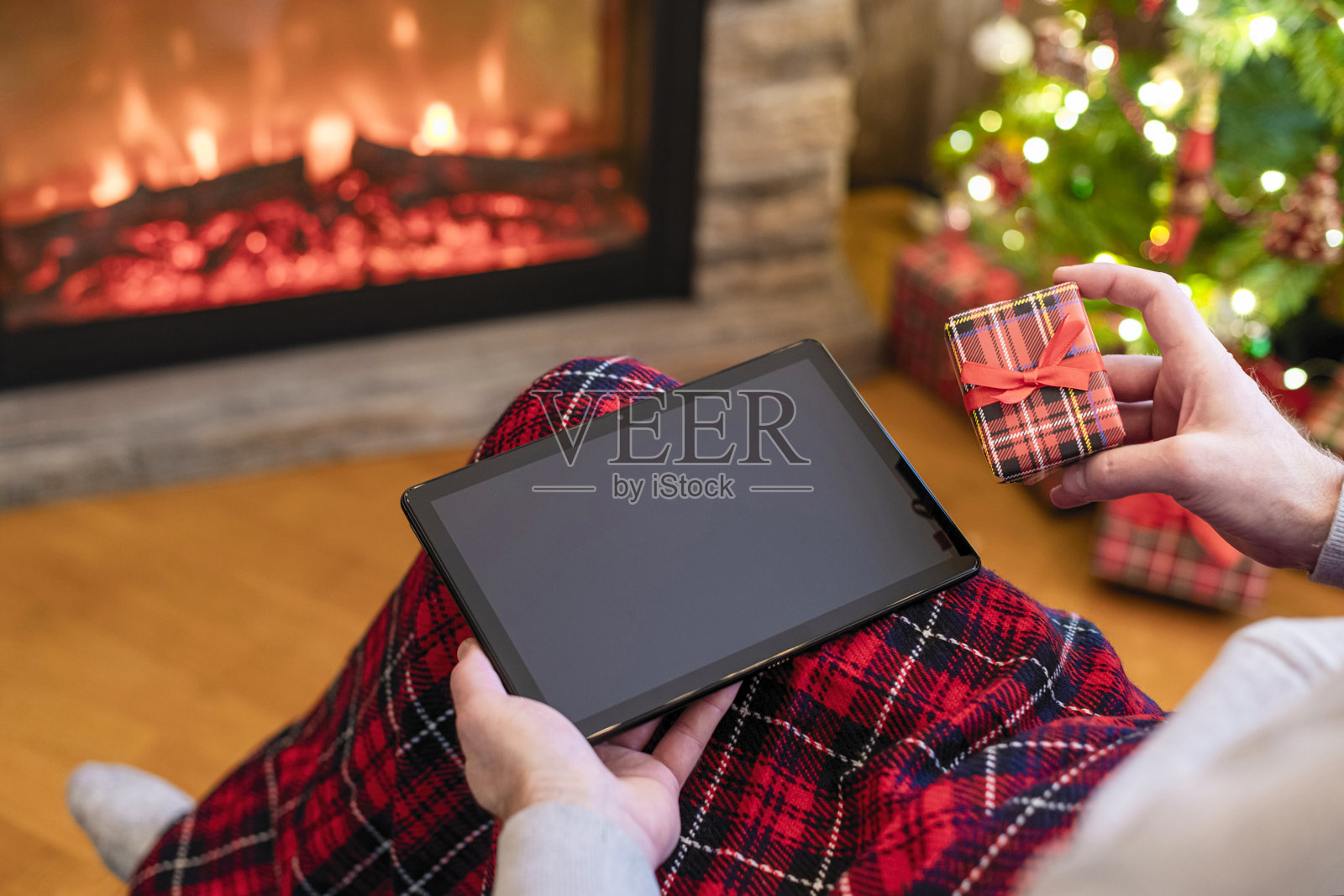 圣诞节。一名男子用平板电脑寻找礼物的想法，坐在壁炉和圣诞树附近准备好的礼物盒。概念照片摄影图片