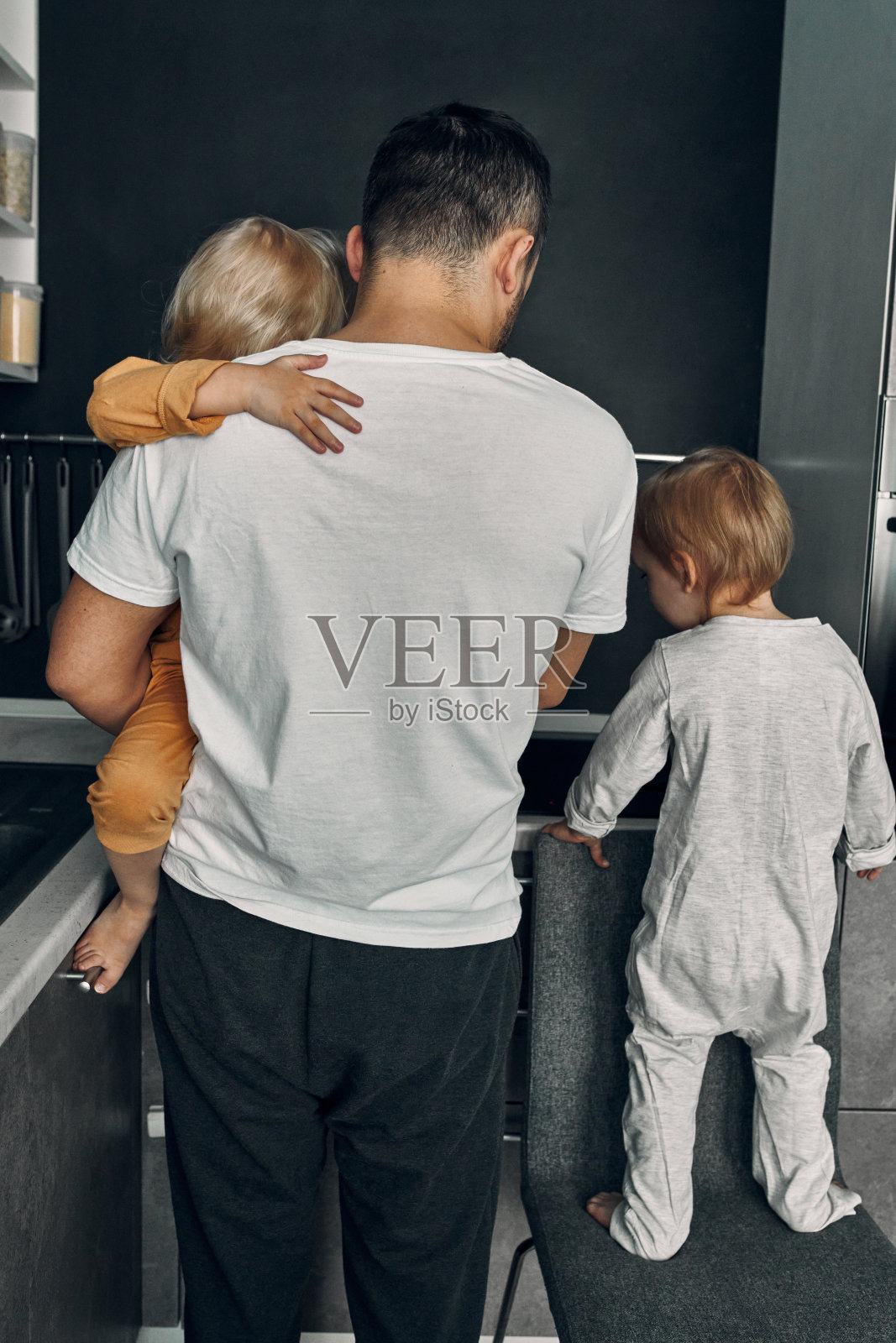 一位年轻的父亲和他的一对三岁的双胞胎，一男一女，正在厨房里准备食物。家庭，孩子，父亲的观念。父亲的一天。生活方式。照片摄影图片