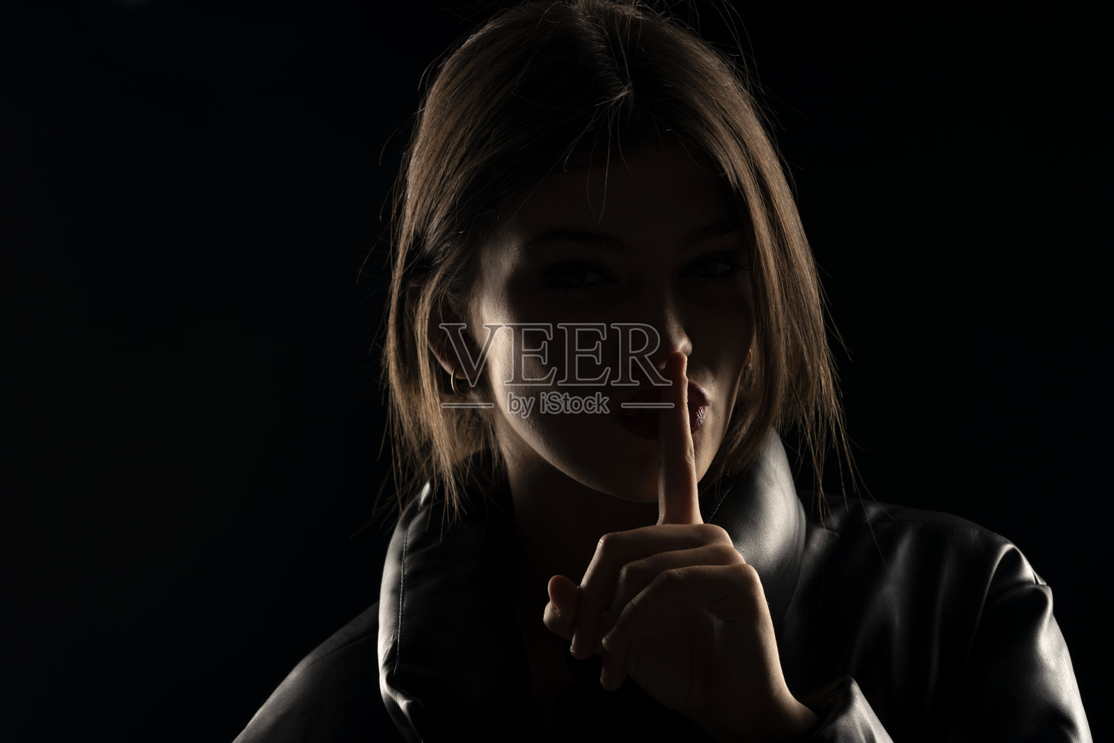 脸上有阴影的女人把手指放在嘴唇上照片摄影图片