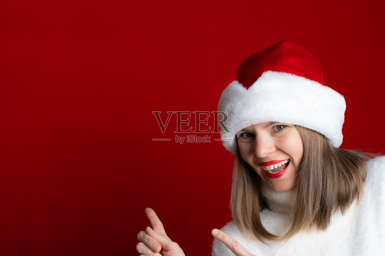 一个穿着白色暖和毛衣、戴着红色圣诞帽的女人用她的手指指着文字或设计的复制空间照片摄影图片