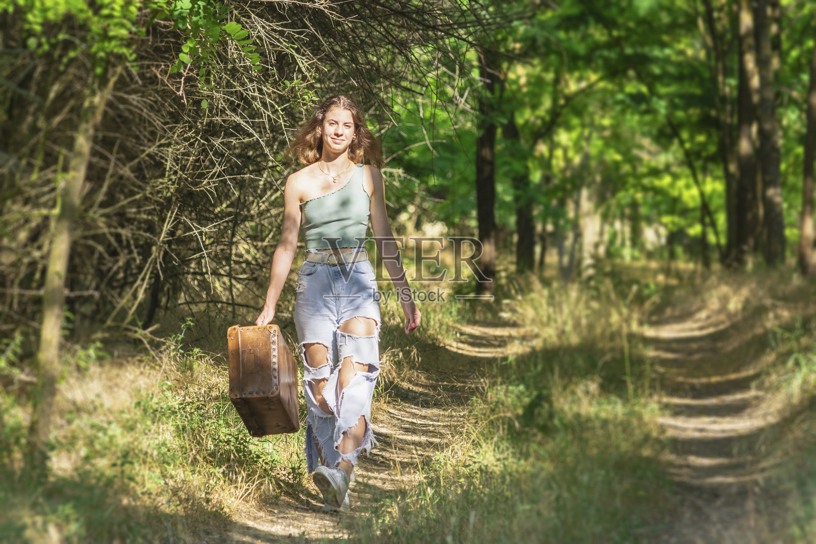 一个女人带着一个旧箱子走在森林路上照片摄影图片