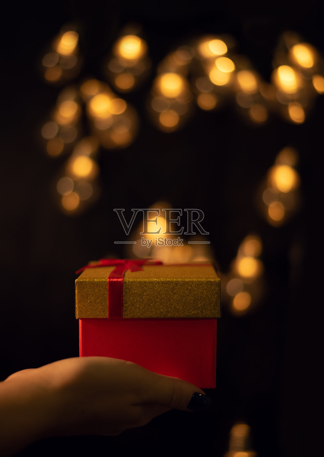 一只手拿着一个礼品盒，背景是暗色的灯光。照片摄影图片