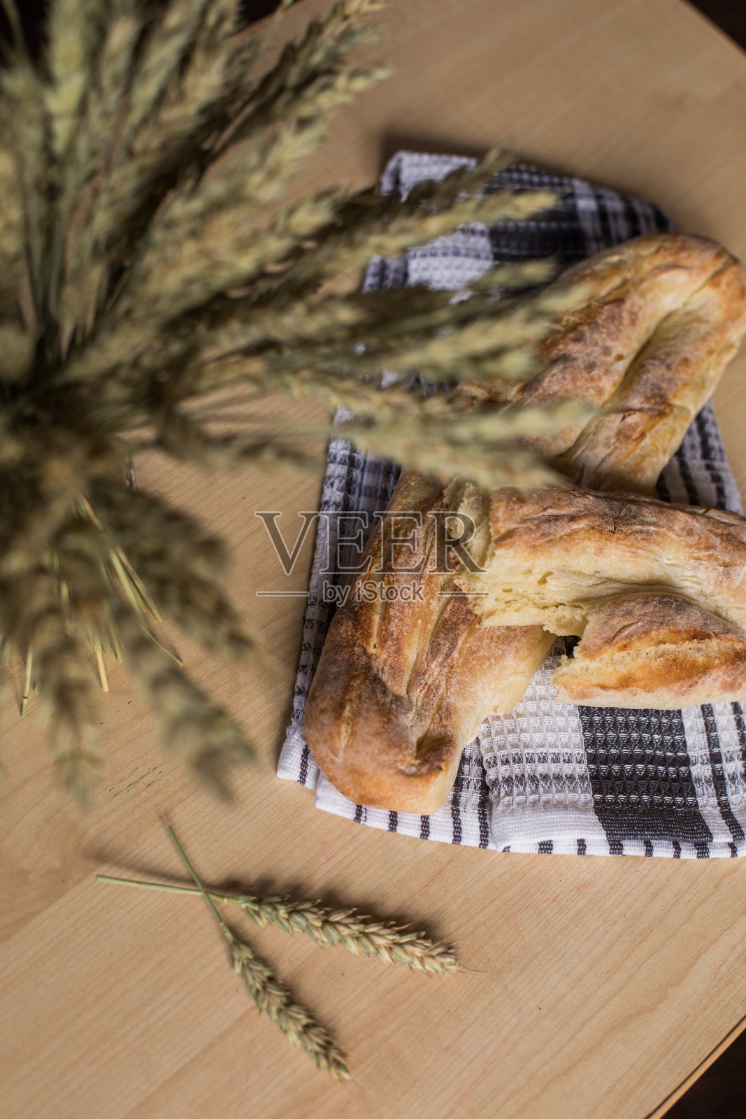 自制面包放在蓝白相间的厨房毛巾上，放在小麦旁边。面包店。新鲜，芳香，热面包照片摄影图片