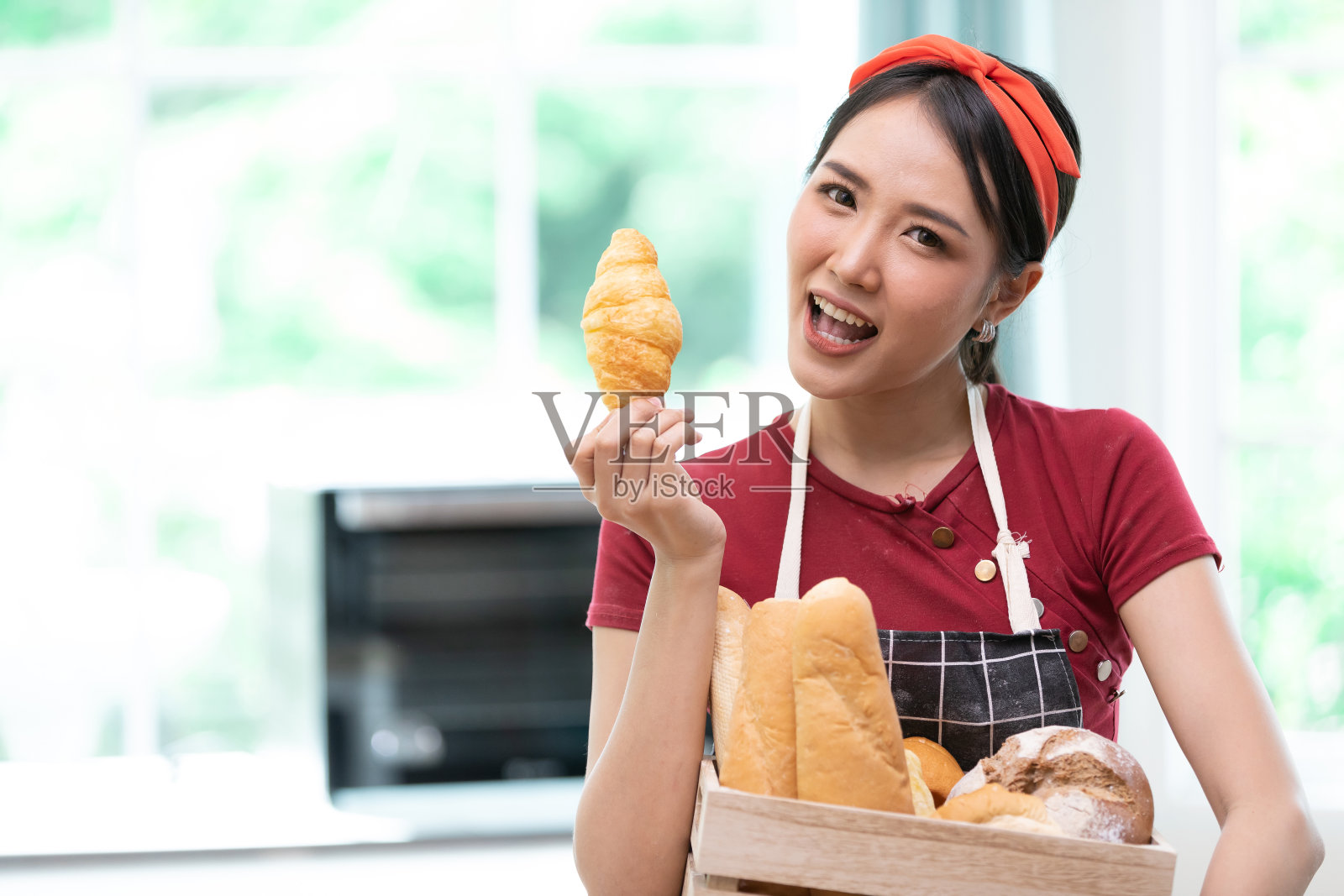 年轻女性家庭主妇拿着牛角面包和面包，为享受在厨房吃照片摄影图片