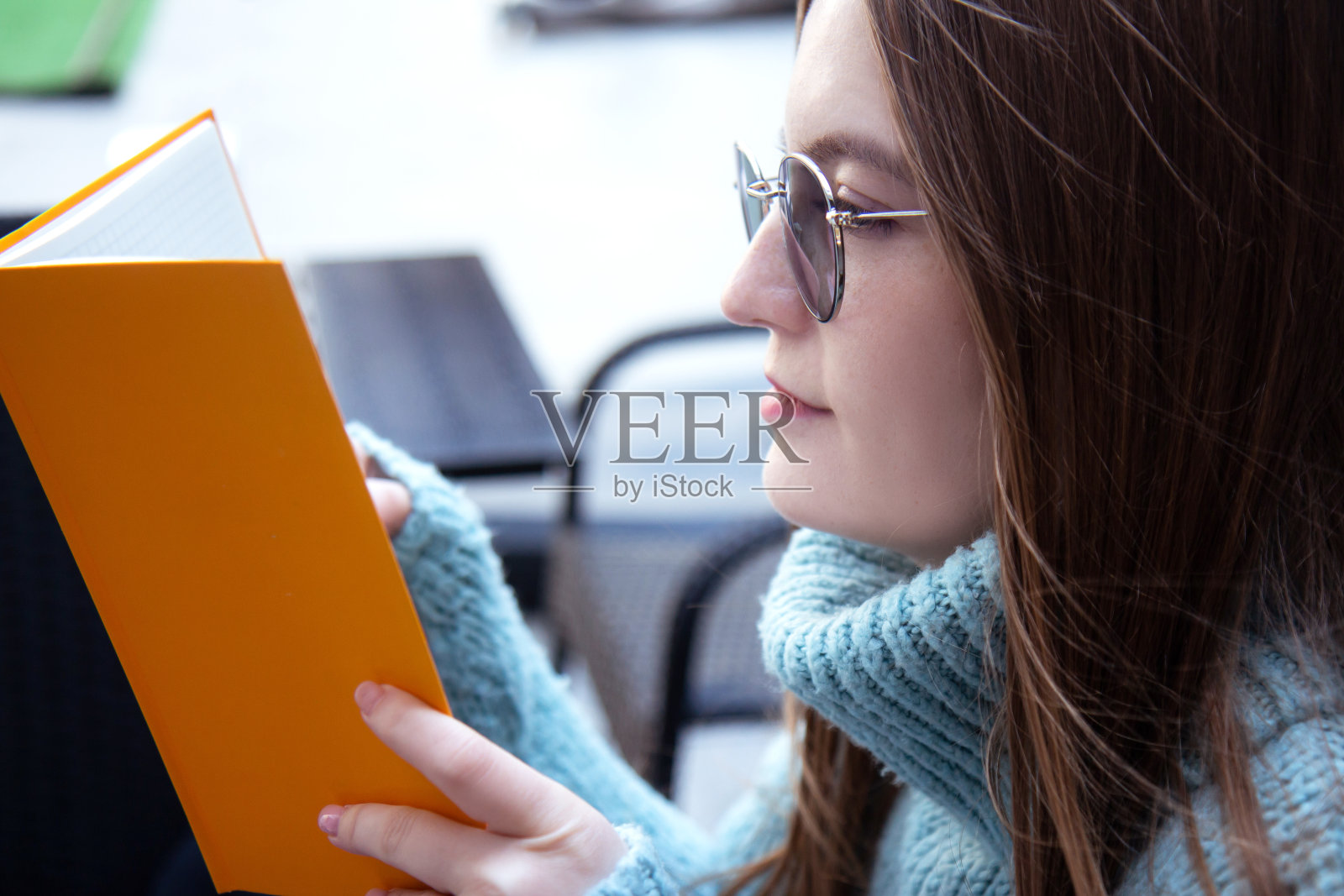 一个长着雀斑戴着眼镜的漂亮女人穿着暖和的毛衣在咖啡馆里看书照片摄影图片