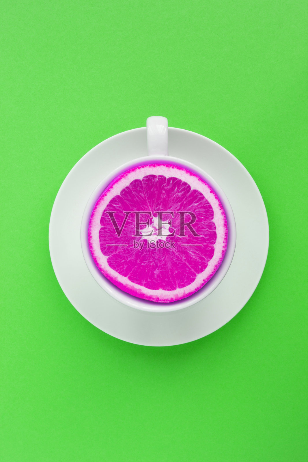 创新食品拼贴。白色茶杯，绿色底色上有粉红色的碎橙。前视图。照片摄影图片