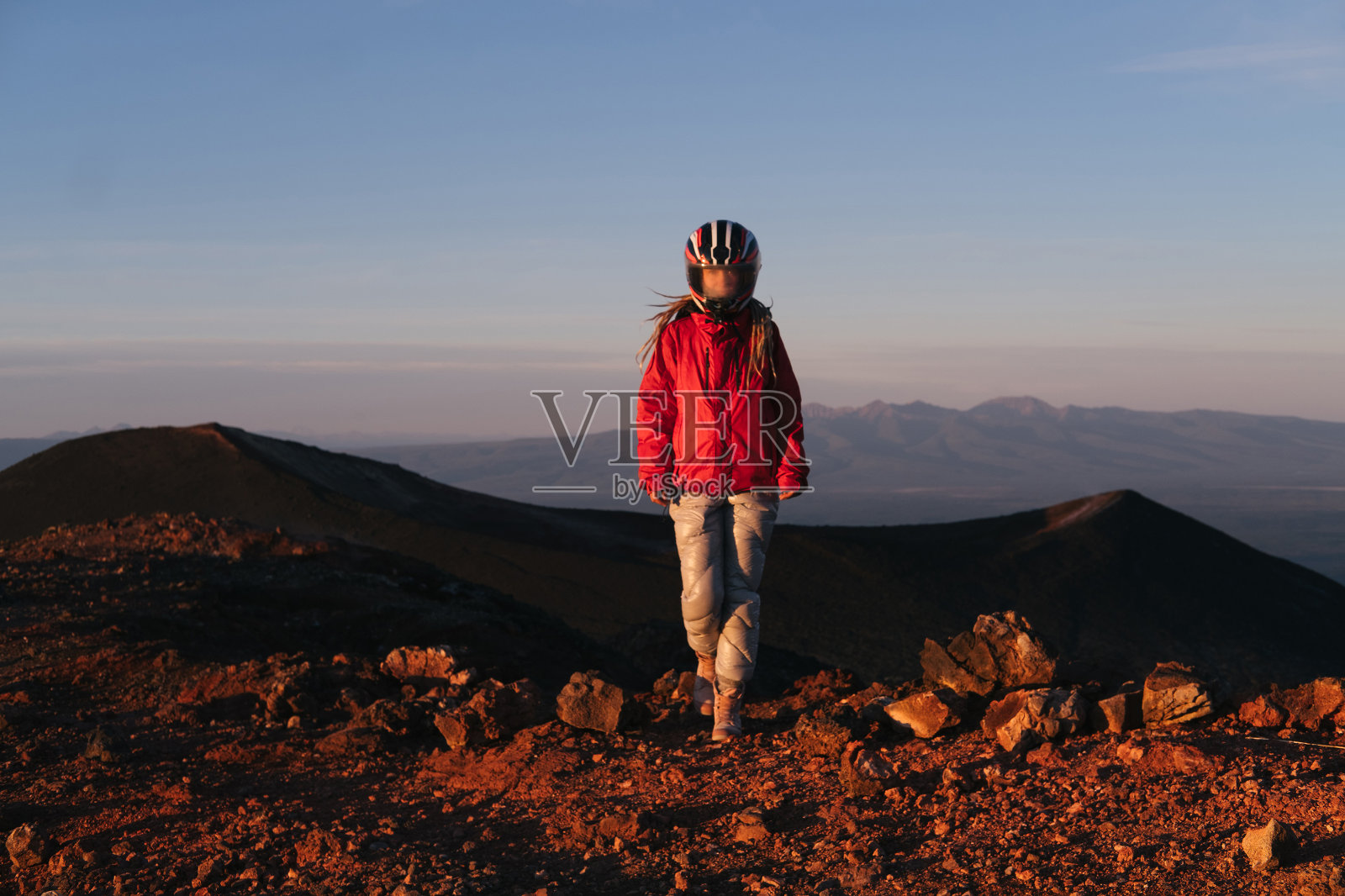 在火山谷戴着摩托车头盔的妇女。雾蒙蒙的玻璃，红色的山丘，就像另一个星球上的火星景观照片摄影图片