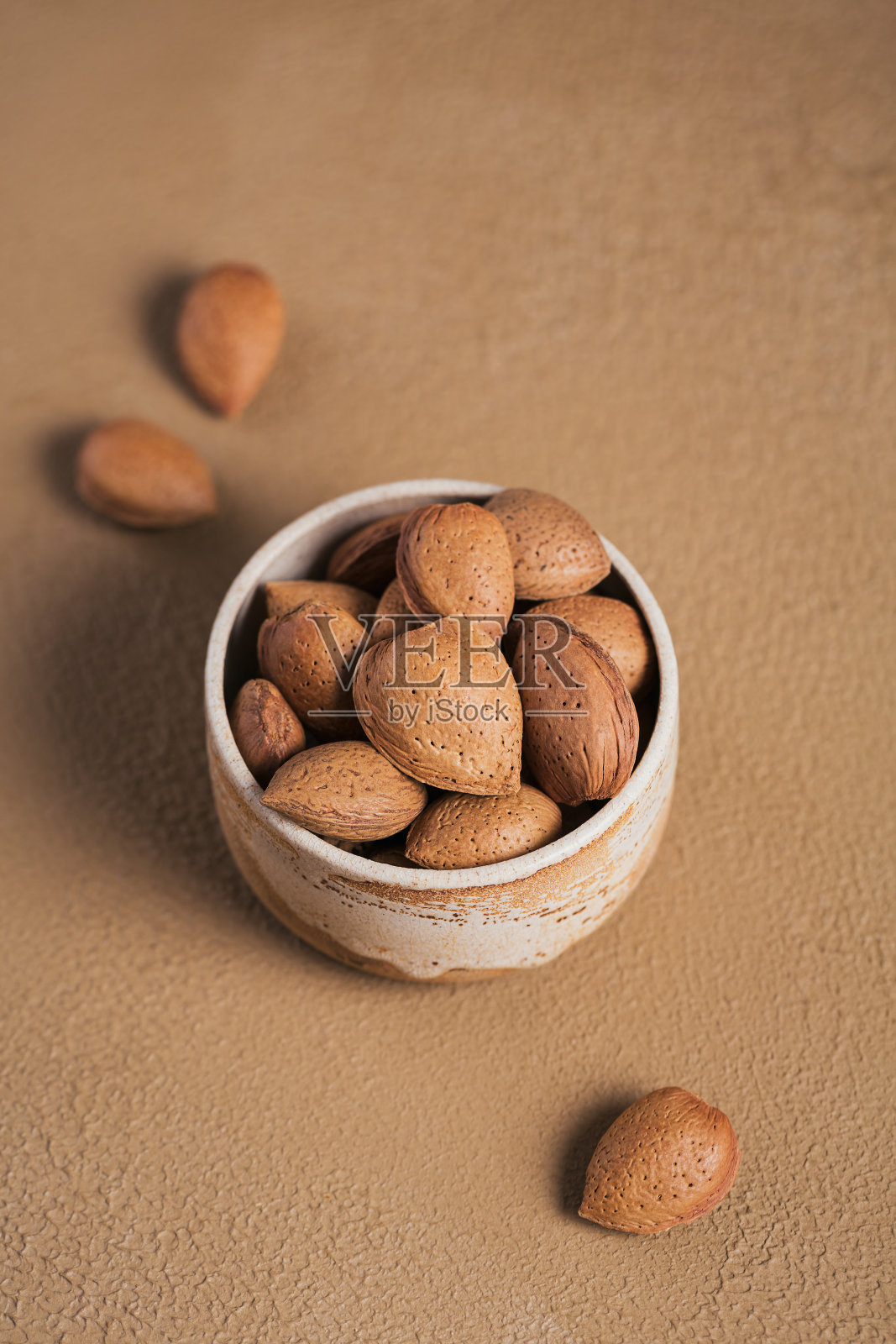 一堆杏仁坚果放在碗里，背景是棕色的。带壳的新鲜坚果。照片摄影图片