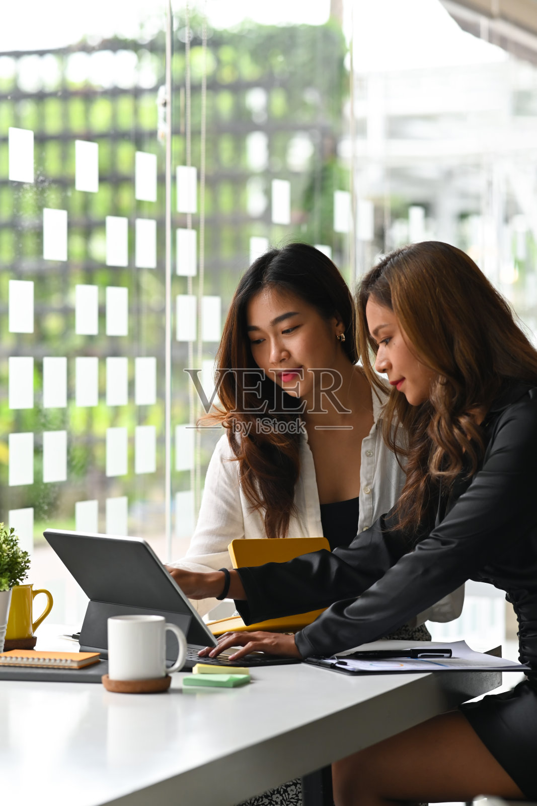 两位女同事在办公室里用平板电脑一起工作。照片摄影图片