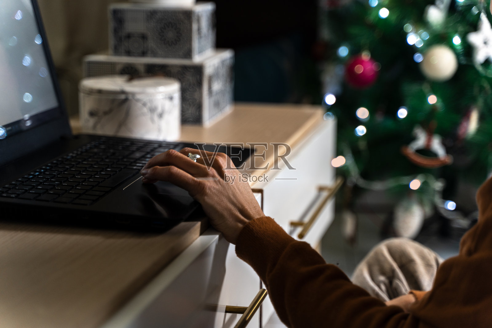 在圣诞树旁边的客厅里，一个女人的手在笔记本电脑上打字。远程办公或圣诞购物的概念照片摄影图片