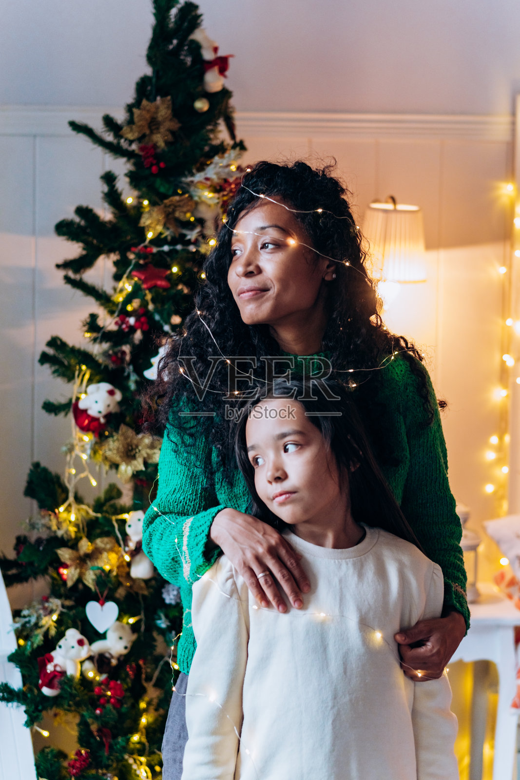 小女孩和妈妈戴着花环对着圣诞树摆姿势照片摄影图片