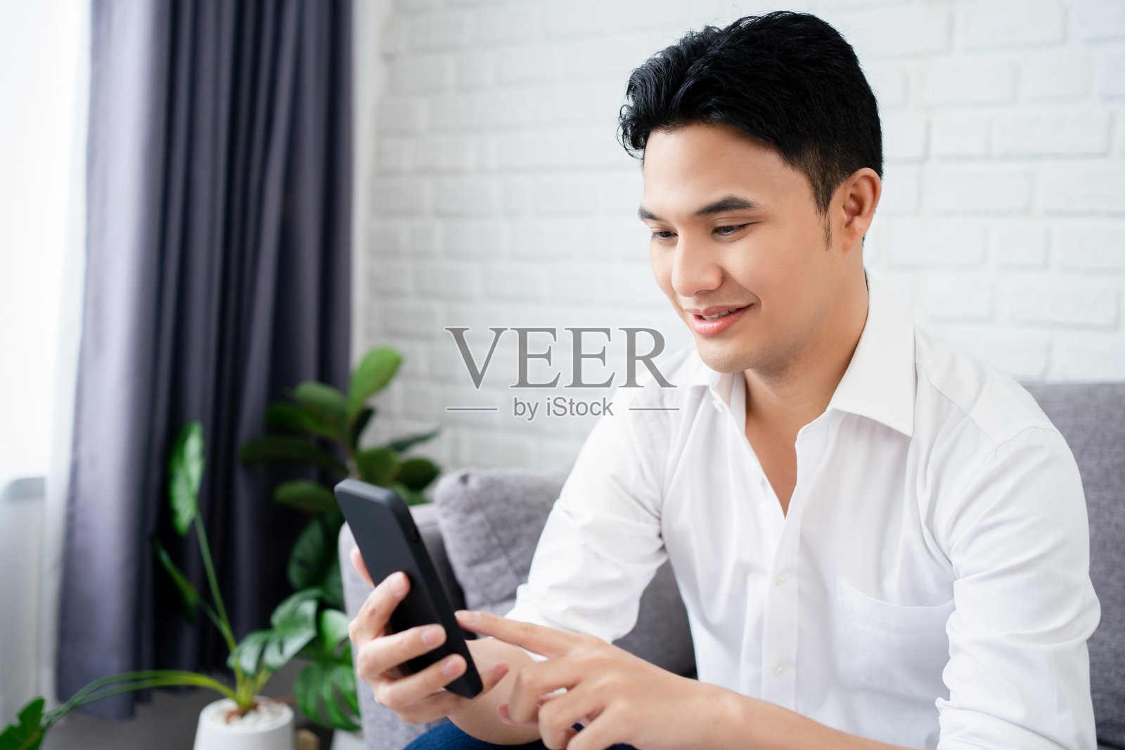 轻松的男人坐在家里的沙发上使用智能手机。照片摄影图片