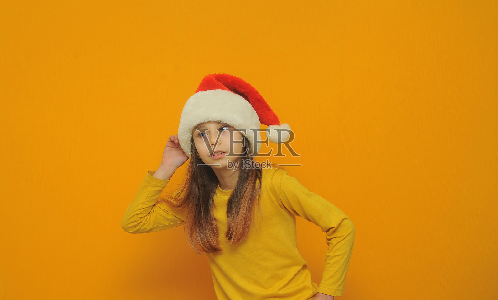 小女孩在圣诞帽在彩色背景与一个复制空间摆姿势。照片摄影图片