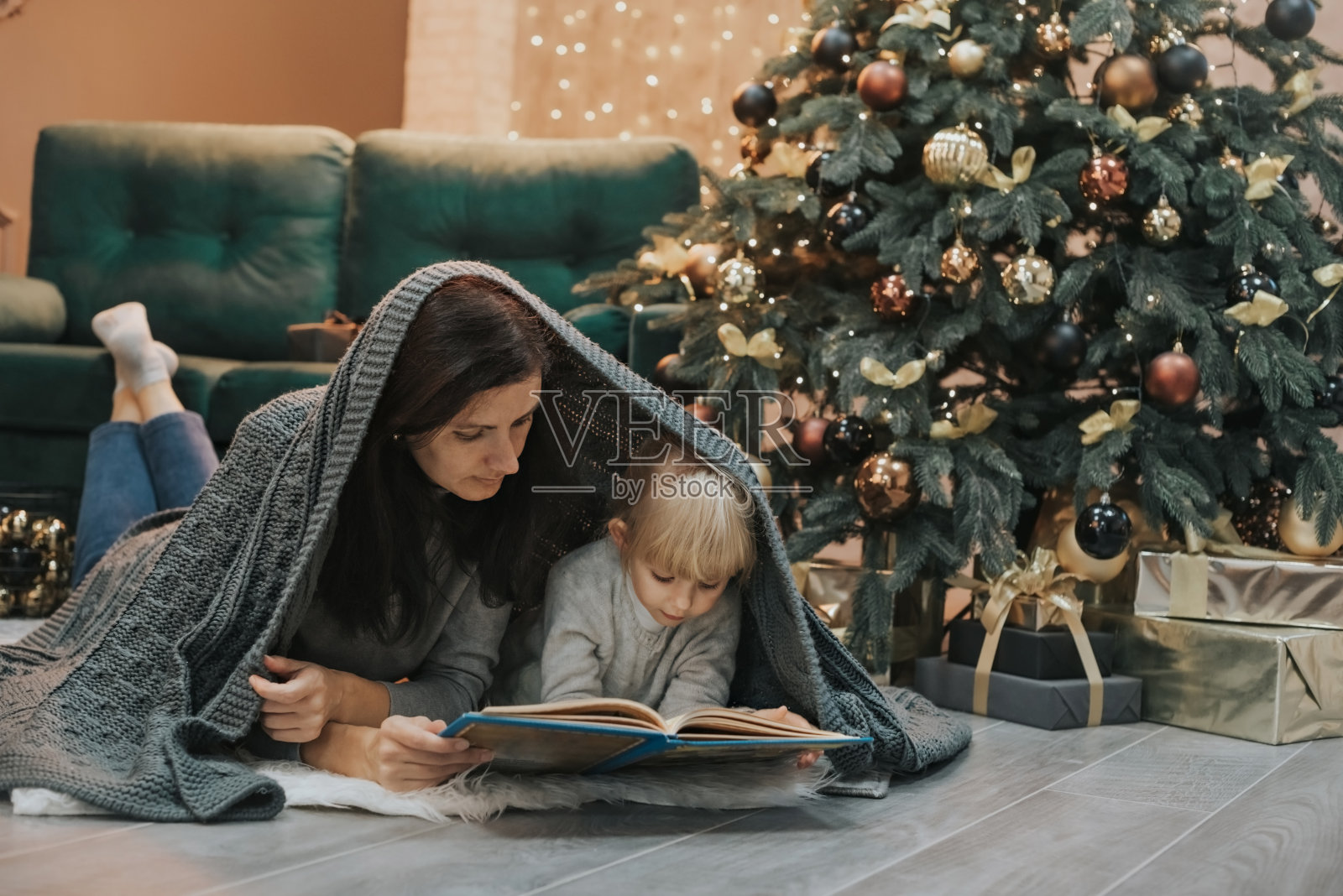 妈妈和女儿躺在圣诞树旁边的地毯上看书照片摄影图片