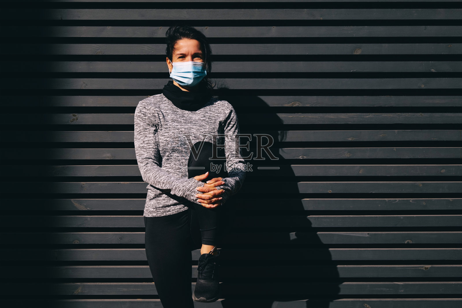 快乐的年轻女子戴着医用口罩在户外伸腿照片摄影图片