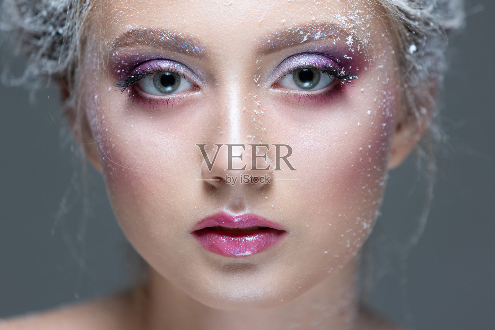 冬天的美丽女人穿着冰冻的花做的衣服，上面覆盖着霜，她的脸和肩膀上有雪。圣诞女孩化妆。给白雪皇后化妆。孤立在灰色背景上。特写镜头照片摄影图片