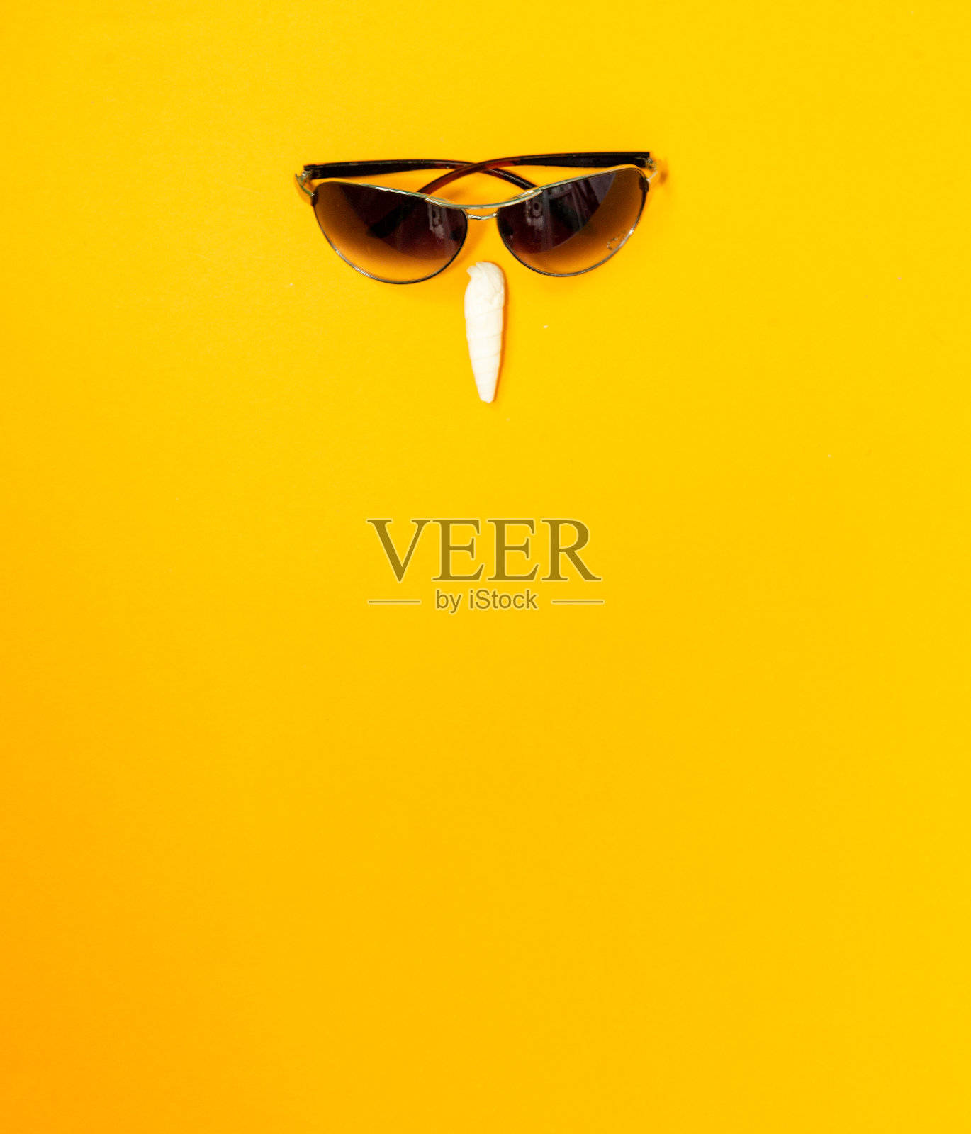 戴着墨镜，明亮的黄色背景上放着一个贝壳。创造性的脸。选择性聚焦，复制空间，横幅照片摄影图片