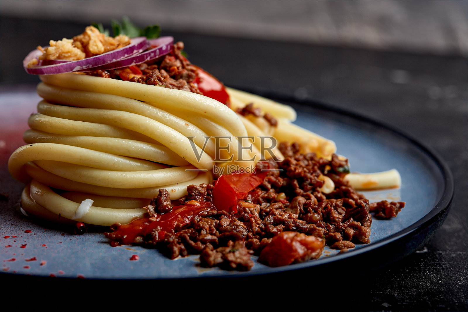 意大利番茄牛肉面。概念意大利菜，漂亮的意大利面放在盘子里，浇上肉酱。蓝色车牌，深色背景照片摄影图片
