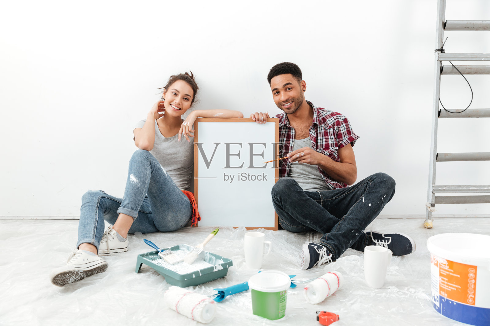 一对夫妇坐在新公寓的地板上拿着写字板。照片摄影图片