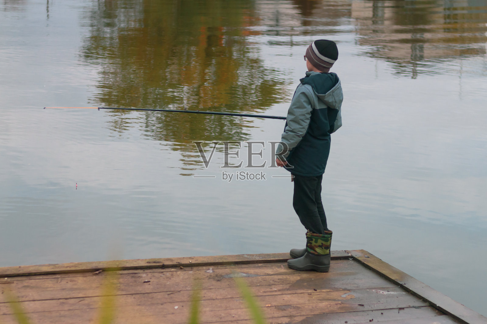 秋天阴天，一个十几岁的男孩在河或湖上用鱼竿钓鱼照片摄影图片