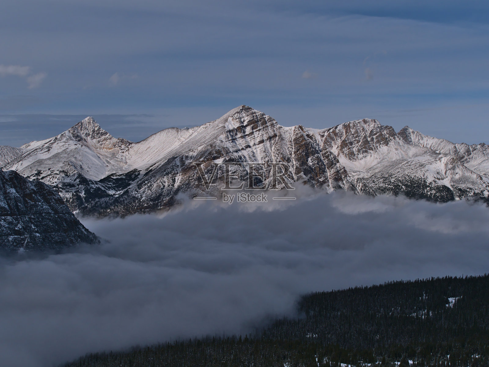 在加拿大阿尔伯塔省的贾斯珀国家公园，积雪覆盖的弗朗切尔峰和雄伟的岩石表面在深秋的云海和森林之上。照片摄影图片