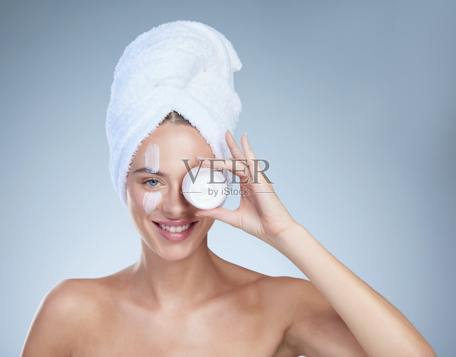 一个迷人的年轻女子的工作室肖像与一个容器的润肤霜在一个灰色的背景照片摄影图片