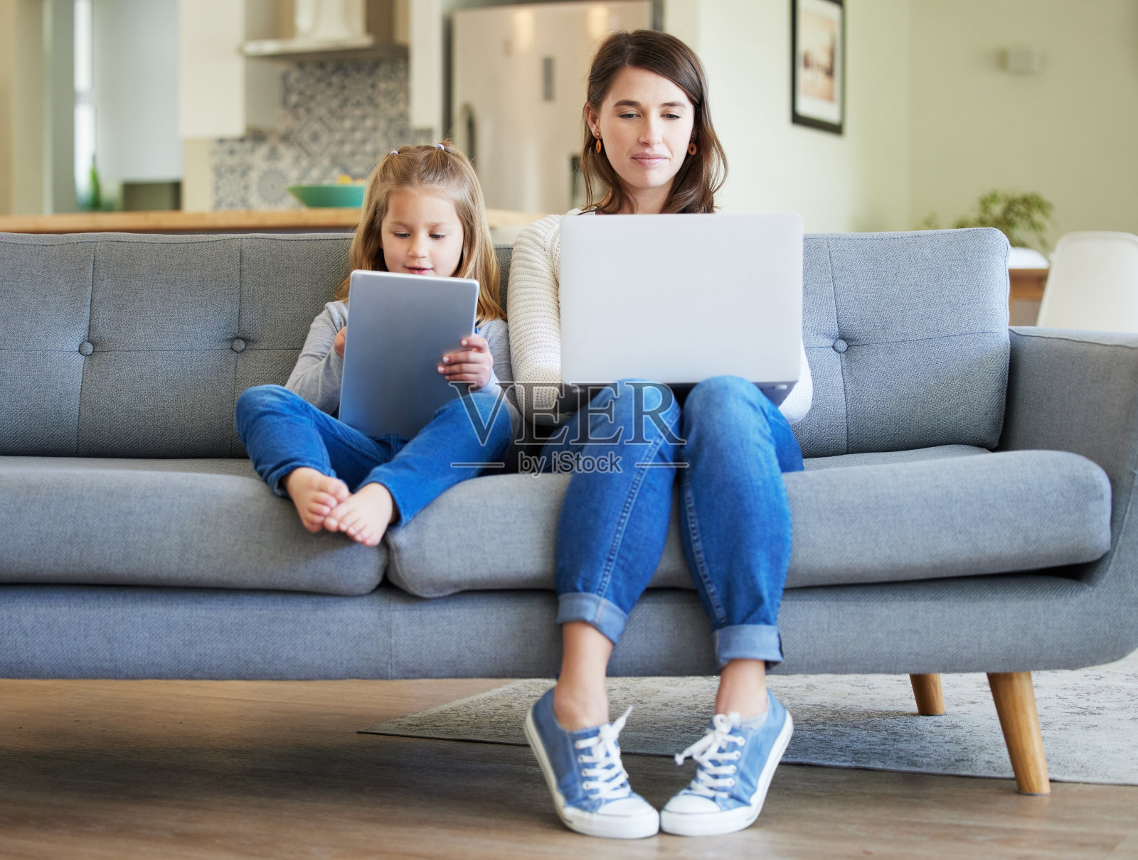 一张年轻的母亲和女儿在家里的沙发上使用笔记本电脑和数码平板电脑的照片照片摄影图片