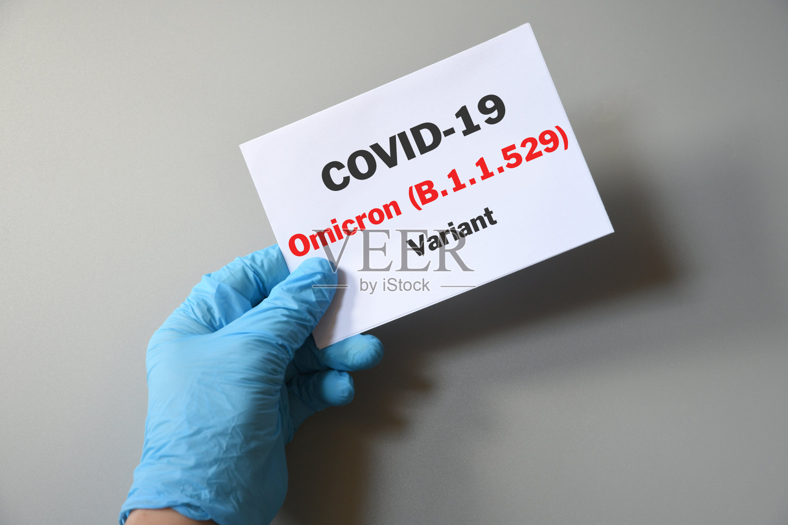 医生的手戴着蓝色手套和白纸，上面写着Covid-19 Omicron变体。医学品种Omicron和COVID-19的概念。COVID-19欧米克隆变体概念。照片摄影图片